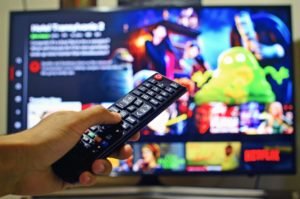 Close up of hand holding TV remote with TV screen in background